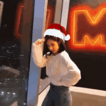 a woman wearing a santa hat is standing in front of a neon m sign