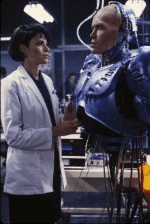 a woman in a white lab coat stands next to a robot