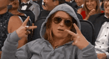 a woman wearing sunglasses and a hoodie is sitting in a crowd of people
