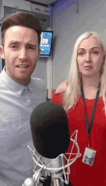 a man and a woman are standing in front of a microphone with a sign on the wall that says now