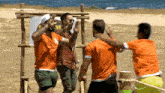 a group of men wearing orange shirts are standing on a beach with a sign in the background that says adventure4asia