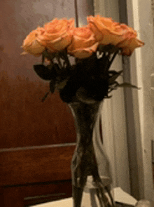 a vase filled with orange roses in front of a wooden door