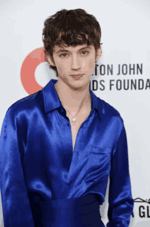 a young man in a blue shirt is standing in front of a sign that says ton john aids founda