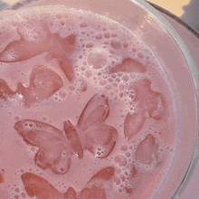 a close up of a pink milkshake with butterfly shaped ice cubes in it .