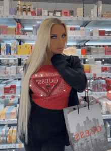 a woman wearing a red guess shirt holds a guess bag