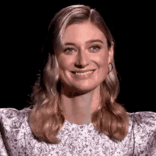 a close up of a woman 's face with a smile on her face . she is wearing a white dress and earrings .