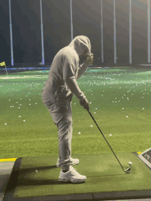 a man in a hoodie is swinging a golf club on a green