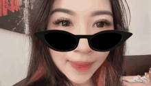 a woman wearing sunglasses looks at the camera in front of a painting that says ' a ' on it