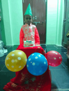 a little boy wearing a party hat stands in front of a cake and balloons