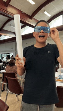 a boy wearing a black under armour shirt is holding a white foam stick