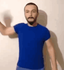a man with a beard and mustache wearing a blue shirt is waving his hand .