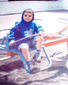 a young boy wearing a blue hoodie is sitting on a seesaw