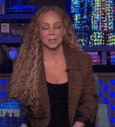 a woman with curly hair wearing a plaid jacket and a black top
