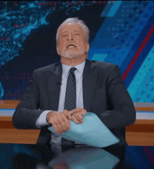 a man in a suit and tie is sitting at a desk with his hands on his head