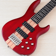 a red bass guitar with the number 5 on the neck sits on a wooden surface