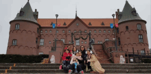 a group of people are posing in front of a large brick building