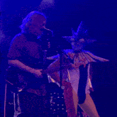 a man playing a guitar next to a man with a mask on playing a guitar