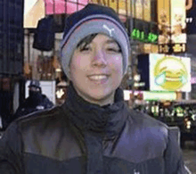 a young man wearing a beanie and a jacket is standing in front of a busy city street .