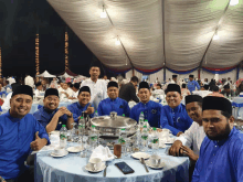 a group of men in blue shirts are sitting at a table in front of a tent