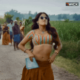a woman wearing sunglasses and a striped top is standing on a dirt road with a wick logo in the corner