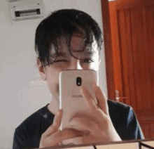 a young man is taking a selfie with his cell phone in a mirror .