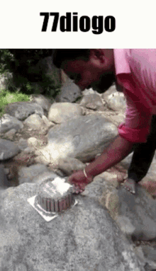 a man in a pink shirt is cutting a cake on a rock with the words 77 diogo above him