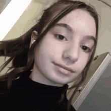 a young girl wearing a black turtleneck and white earbuds looks at the camera