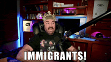 a man sitting in front of a microphone with the word immigrants on his shirt