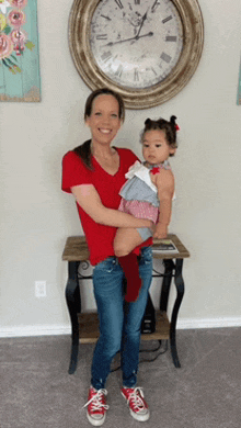 a woman holding a little girl in front of a clock