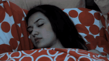 a woman is sleeping in a bed with a red and white polka dot blanket