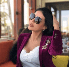 a woman wearing a purple jacket and sunglasses has a chanel brooch on her jacket