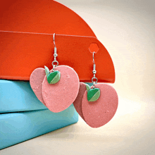 a pair of pink apple shaped earrings are hanging from a hook