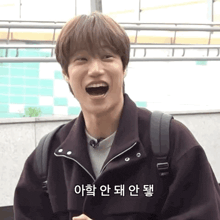 a young man is laughing with his mouth open while wearing a jacket and a backpack .