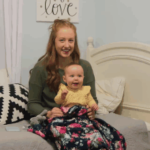 a woman is holding a baby in front of a sign that says " love "