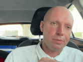 a bald man in a white shirt is sitting in the driver 's seat of a car