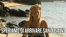 a woman wearing a flower crown is standing on a beach with the words speriamo di arrivare sani e salvi above her