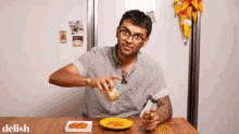 a man is sitting at a table with a plate of food and the word delish on the bottom right