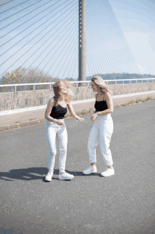 two women are standing on a street with a bridge in the background