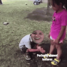 a girl in a pink shirt is kneeling down next to a boy with a picture of a woman 's face on his head