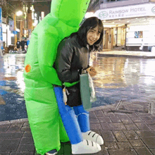 a woman is being hugged by a green inflatable person in front of a rainbow hotel