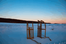 two wooden sleds are sitting in a snowy field at sunset