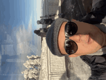 a man wearing sunglasses and a hat stands in front of a snowy fence