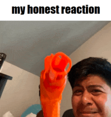 a man is holding an orange nerf gun in front of a sign that says " my honest reaction "