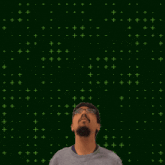 a man wearing glasses stands in front of a green background with the number 7 + 0 above him