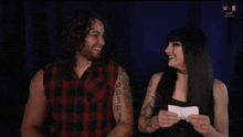 a man and a woman are laughing in front of a screen that says w live