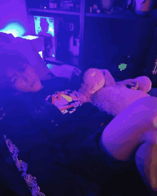 a person laying on a bed with a teddy bear and a purple light behind them that says glow in the dark