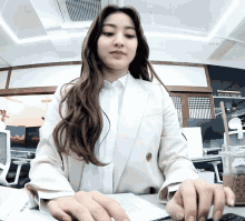 a woman in a white suit sits at a desk with a cup of collect time in front of her