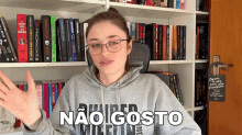 a woman wearing a hoodie that says " não gosto " stands in front of a bookshelf full of books