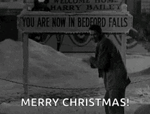 a man is standing in the snow with his arms in the air in front of a sign that says merry christmas .