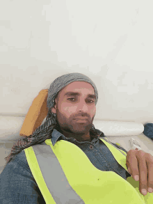 a man wearing a yellow vest and a head scarf looks at the camera